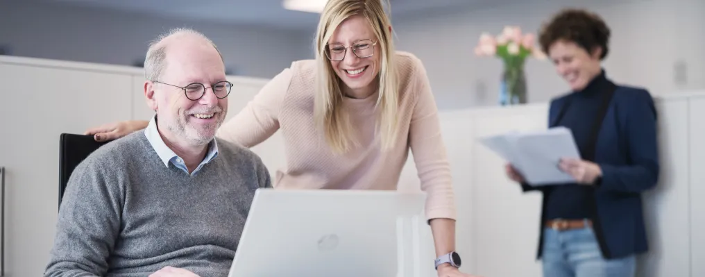 two people in the office with laptop, one person in the back