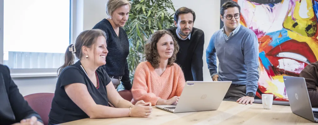 five people around a laptop in a meeting room