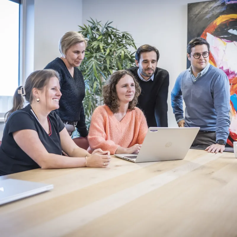 five people around a laptop in a meeting room