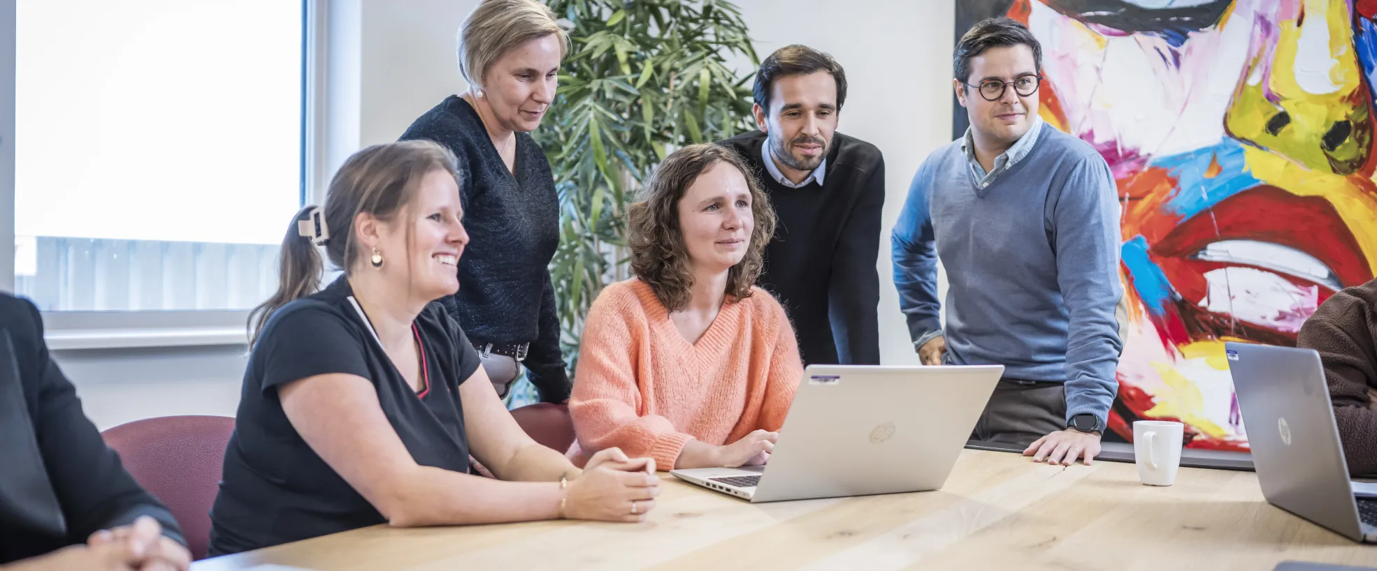 five people around a laptop in a meeting room
